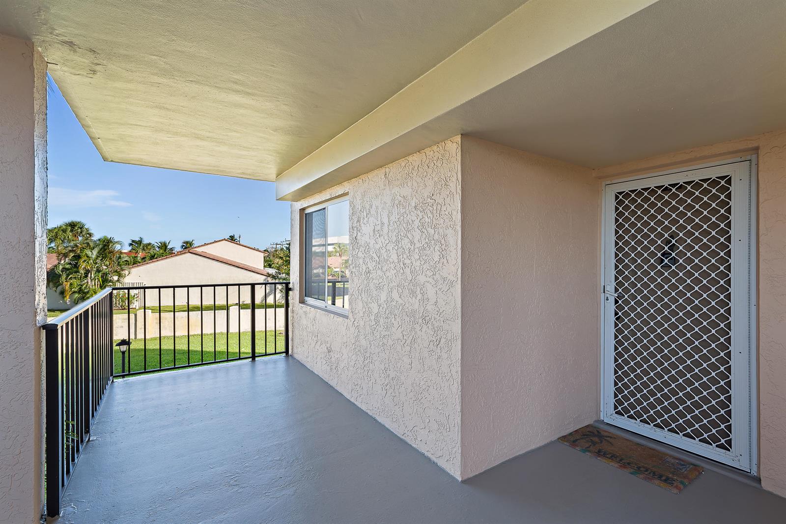 A covered balcony with a grey floor, black metal railing, and a white screen door — 275 Palm Avenue # C201, Jupiter FL 33477, JUPITER, FL