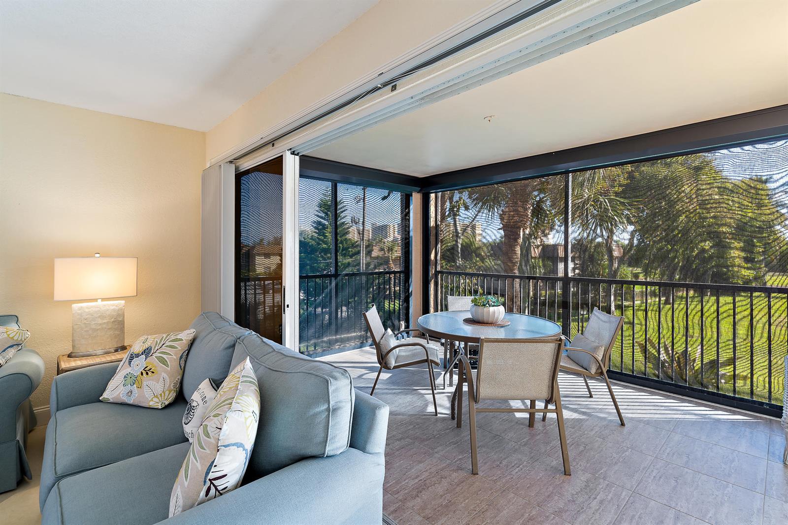 A blue sofa sits in a living room opening to a screened-in balcony with dining furniture — 275 Palm Avenue # C201, Jupiter FL 33477, JUPITER, FL
