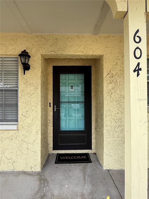 A yellow stucco exterior features a dark front door with a glass insert and welcome mat — 2465 NORTHSIDE DRIVE UNIT 604, CLEARWATER, FL