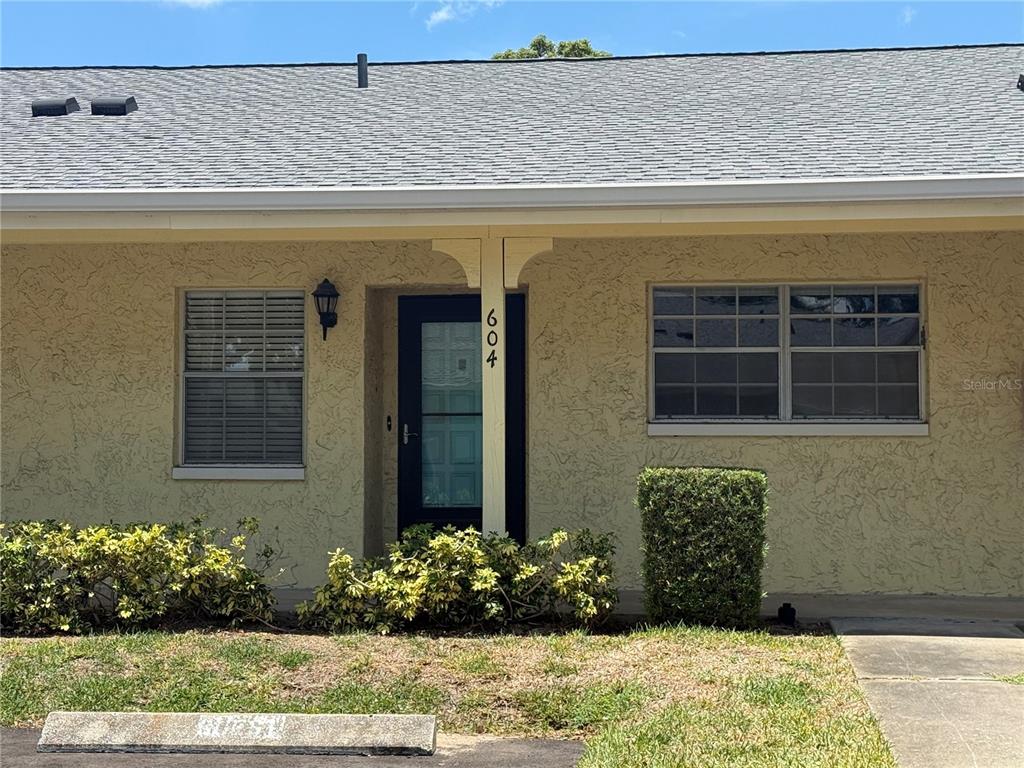 The exterior of a single-story home features a tan stucco facade, a dark front door, and windows — 2465 NORTHSIDE DRIVE UNIT 604, CLEARWATER, FL