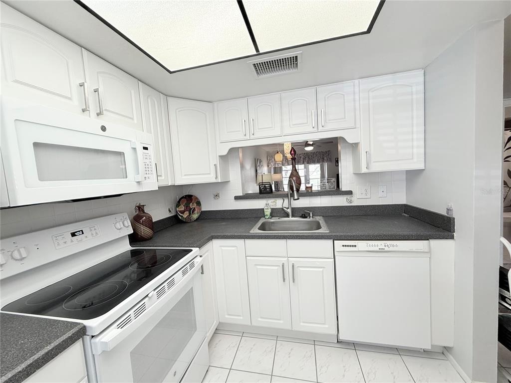 A kitchen with white cabinets, dark countertops, white appliances, and a pass-through window — 2465 NORTHSIDE DRIVE UNIT 604, CLEARWATER, FL