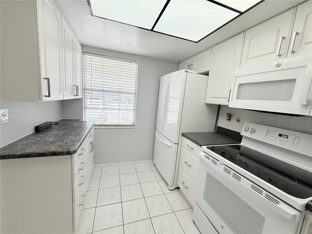 A galley kitchen features white cabinets, dark countertops, white appliances, and tiled flooring — 2465 NORTHSIDE DRIVE UNIT 604, CLEARWATER, FL