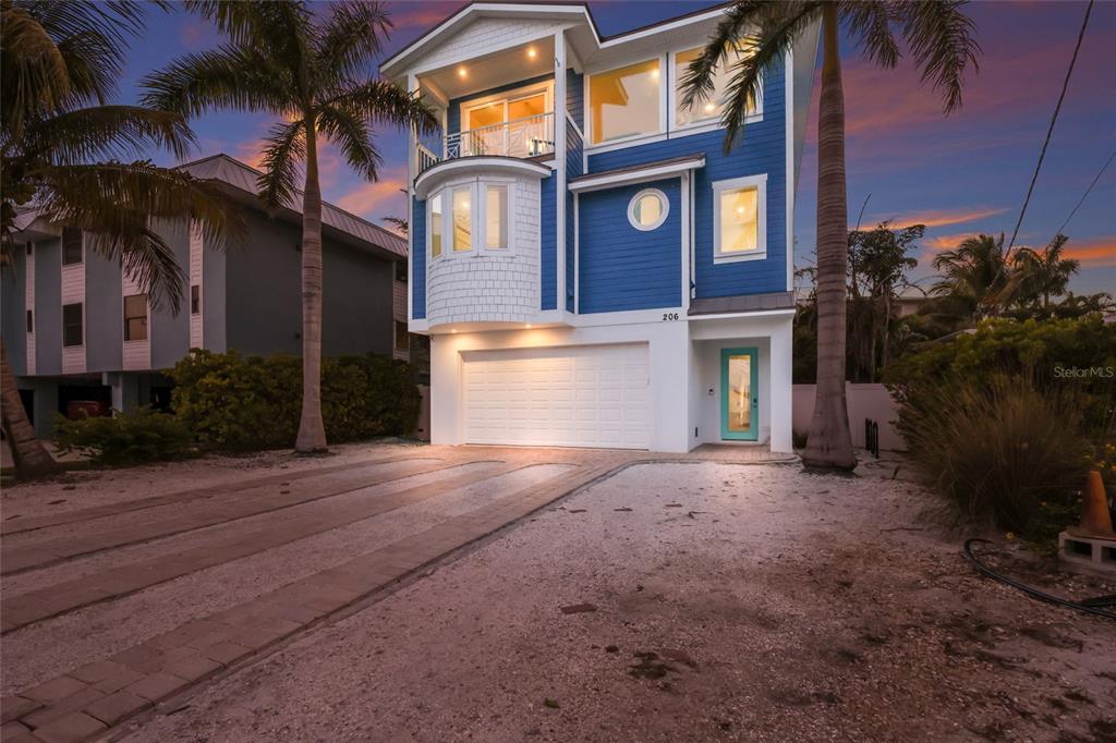 A three-story blue house with a white garage and a teal front door at dusk — 206 CHURCH AVENUE, BRADENTON BEACH, FL