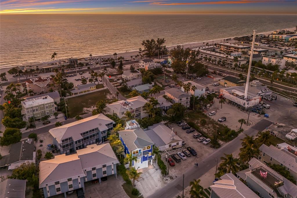 An aerial view shows a blue multi-story house near a beach at sunset — 206 CHURCH AVENUE, BRADENTON BEACH, FL