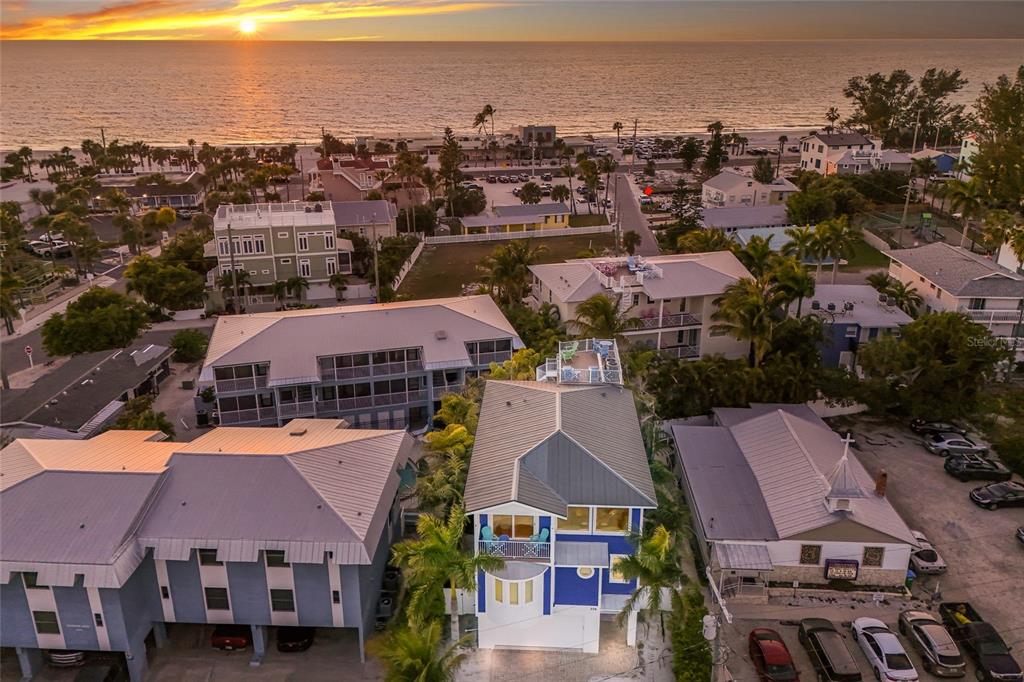 An aerial view shows a blue beach house with a rooftop deck near the ocean — 206 CHURCH AVENUE, BRADENTON BEACH, FL