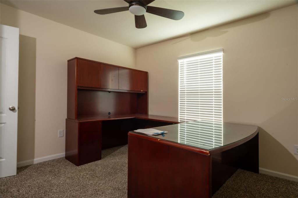 A home office features a large L-shaped wooden desk with a hutch and carpeted flooring — 32 ROYAL OAK DRIVE, PALM COAST, FL