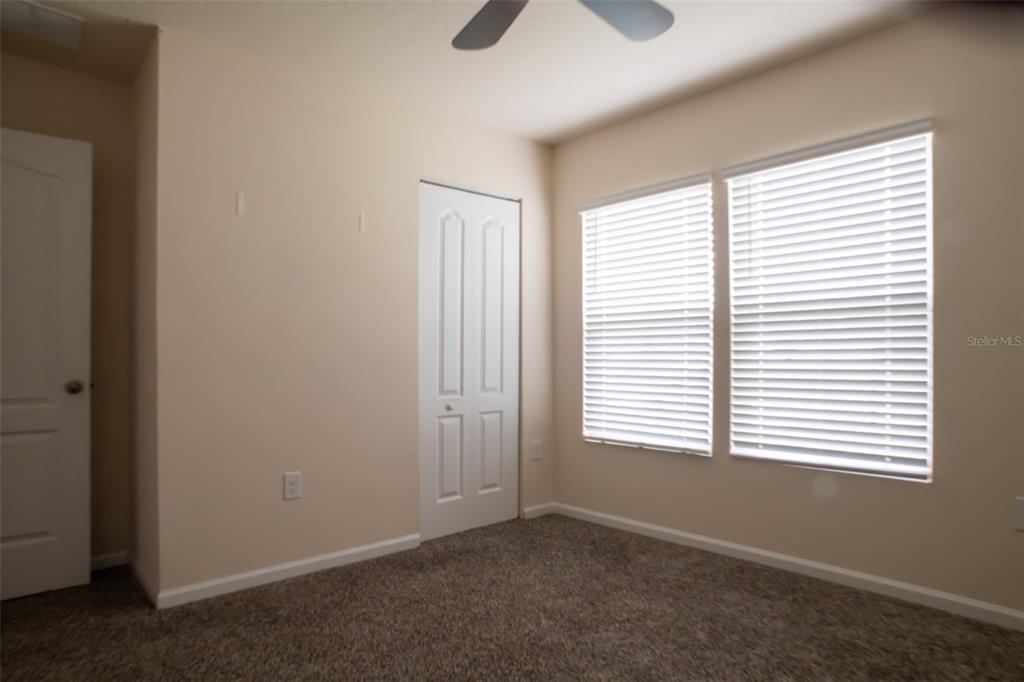 An empty bedroom features beige walls, brown carpet, a ceiling fan, and two windows — 32 ROYAL OAK DRIVE, PALM COAST, FL