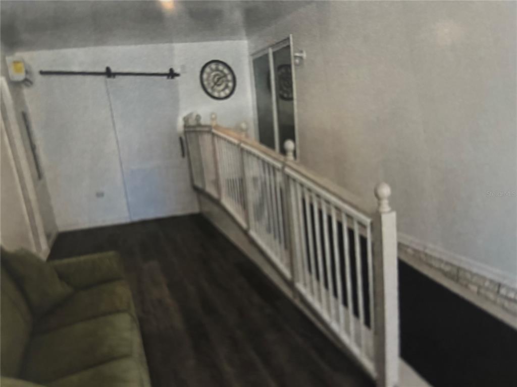 A room with dark wood-look flooring, a green sofa, and a white wooden stair railing — 4325 WATER OAK LANE UNIT 54, ZELLWOOD, FL