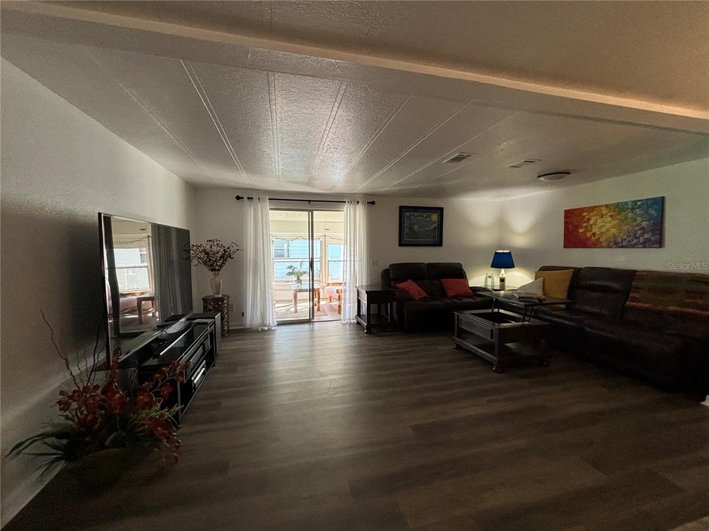 A living room features wood-look flooring, a large television, and a sliding door to a porch — 4325 WATER OAK LANE UNIT 54, ZELLWOOD, FL