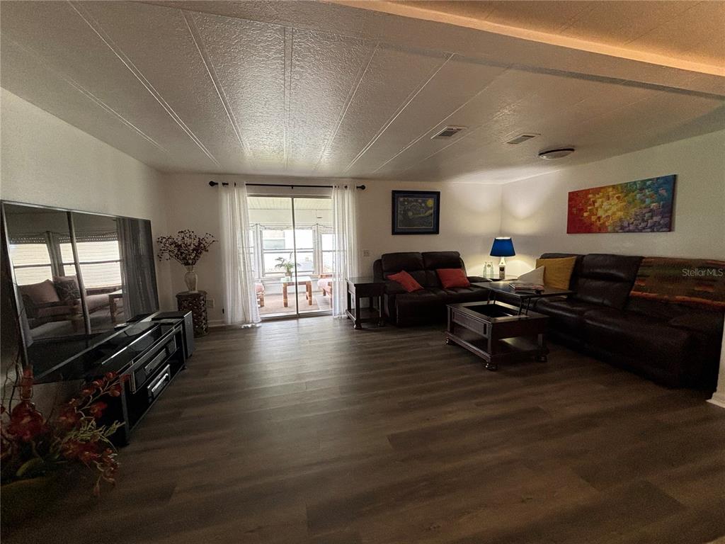 A living room features dark wood-look flooring, leather sofas, a large television, and sliding glass doors — 4325 WATER OAK LANE UNIT 54, ZELLWOOD, FL