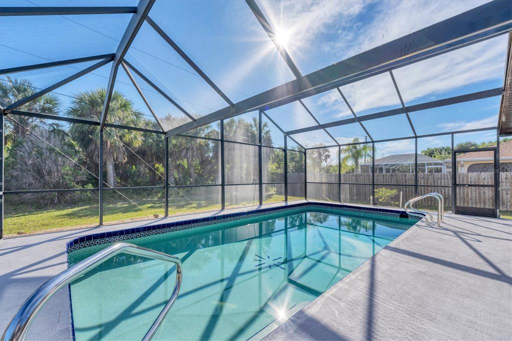 A rectangular swimming pool is enclosed by a screened lanai with a concrete deck — 18091 EAU GALLIE CIRCLE, PORT CHARLOTTE, FL