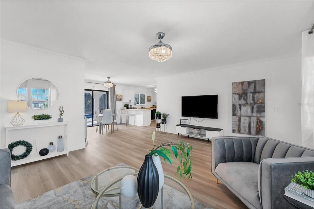 A bright, open-concept living room features light wood flooring, a modern chandelier, and white walls — 18091 EAU GALLIE CIRCLE, PORT CHARLOTTE, FL