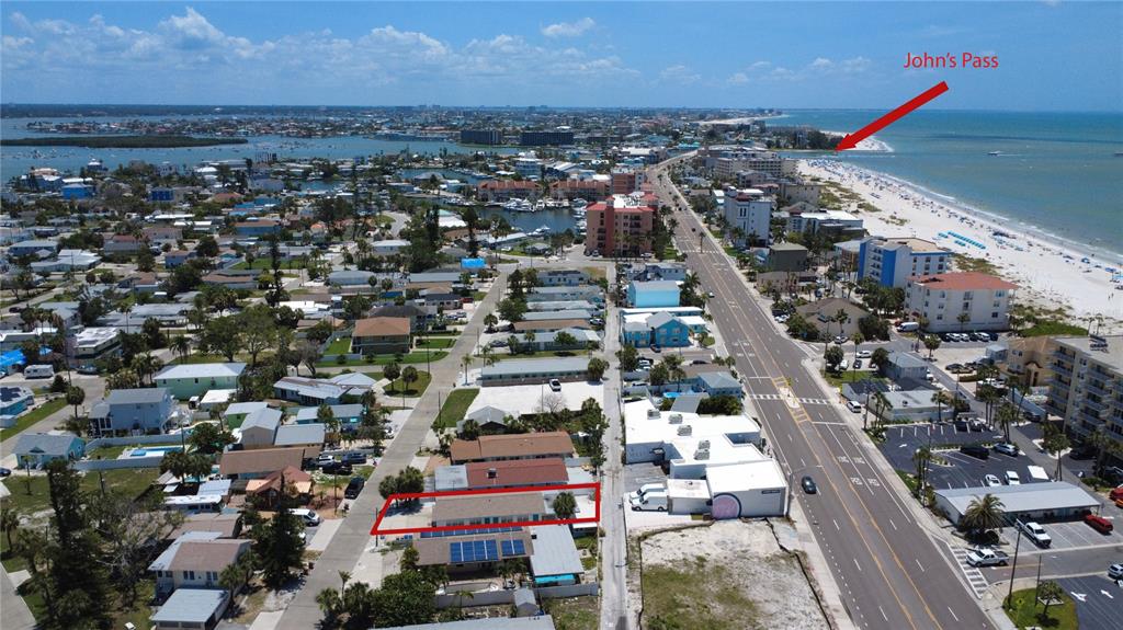 An aerial view shows a coastal neighborhood with a red-outlined building near a beach — 13440 1ST STREET E, MADEIRA BEACH, FL