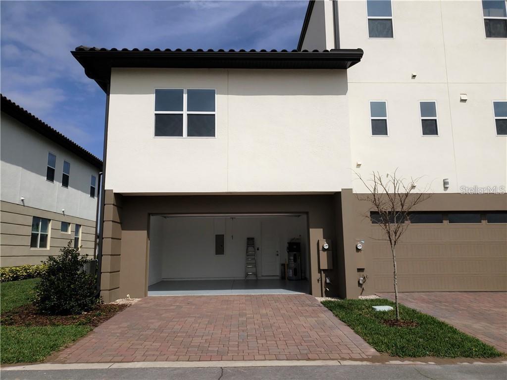 An exterior view of a two-story townhouse featuring an open garage and paved driveway — 9467 MERE PARKWAY, ORLANDO, FL