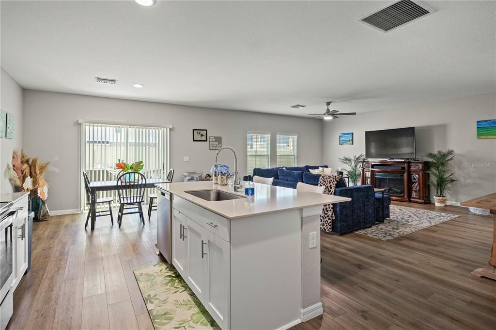 An open-concept kitchen with a central island overlooks a living area and dining space — 7580 FREESIA TRACE, WESLEY CHAPEL, FL
