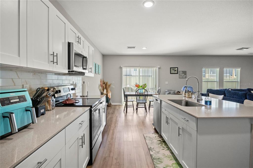 A modern kitchen features white cabinetry, quartz countertops, stainless steel appliances, and wood-look flooring — 7580 FREESIA TRACE, WESLEY CHAPEL, FL