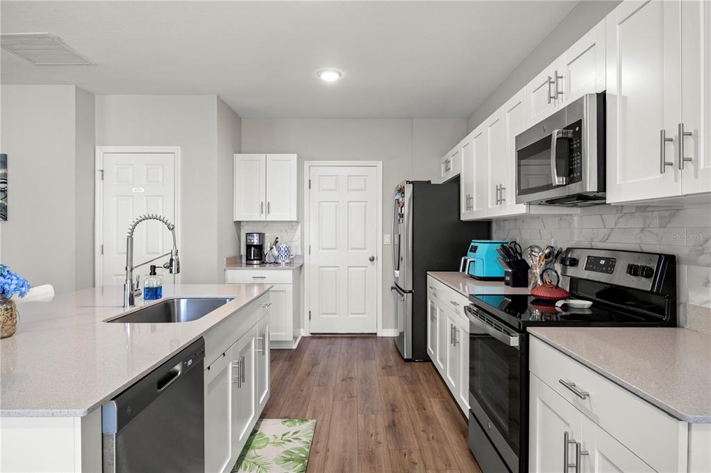 A modern kitchen features white cabinets, stainless steel appliances, and a large central island — 7580 FREESIA TRACE, WESLEY CHAPEL, FL
