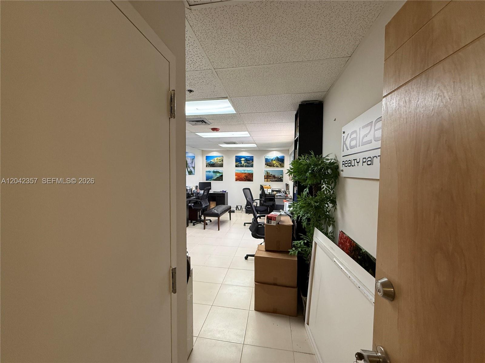 An office space features tiled floors, desks, chairs, and wall art under drop ceiling panels — 9600 NW 25th St # 4H, Doral FL 33172, DORAL, FL