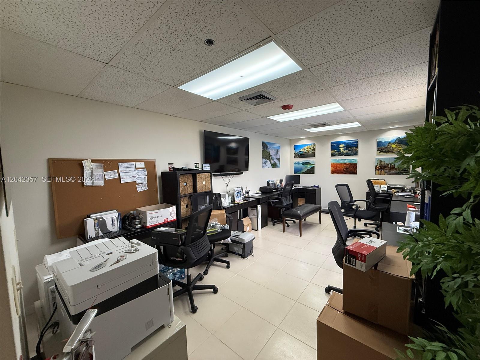 An office space features multiple desks, rolling chairs, a wall-mounted television, and tiled flooring — 9600 NW 25th St # 4H, Doral FL 33172, DORAL, FL