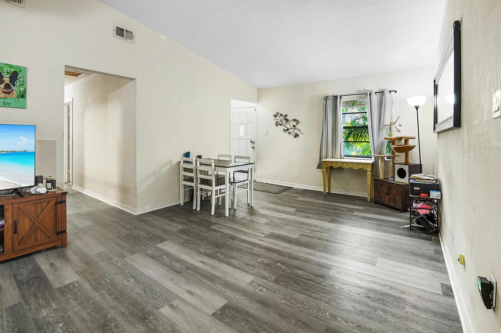 This room features gray wood-look flooring, a dining set, a television, and a window — 203 E Easy Street, Fort Pierce FL 34982, FORT PIERCE, FL