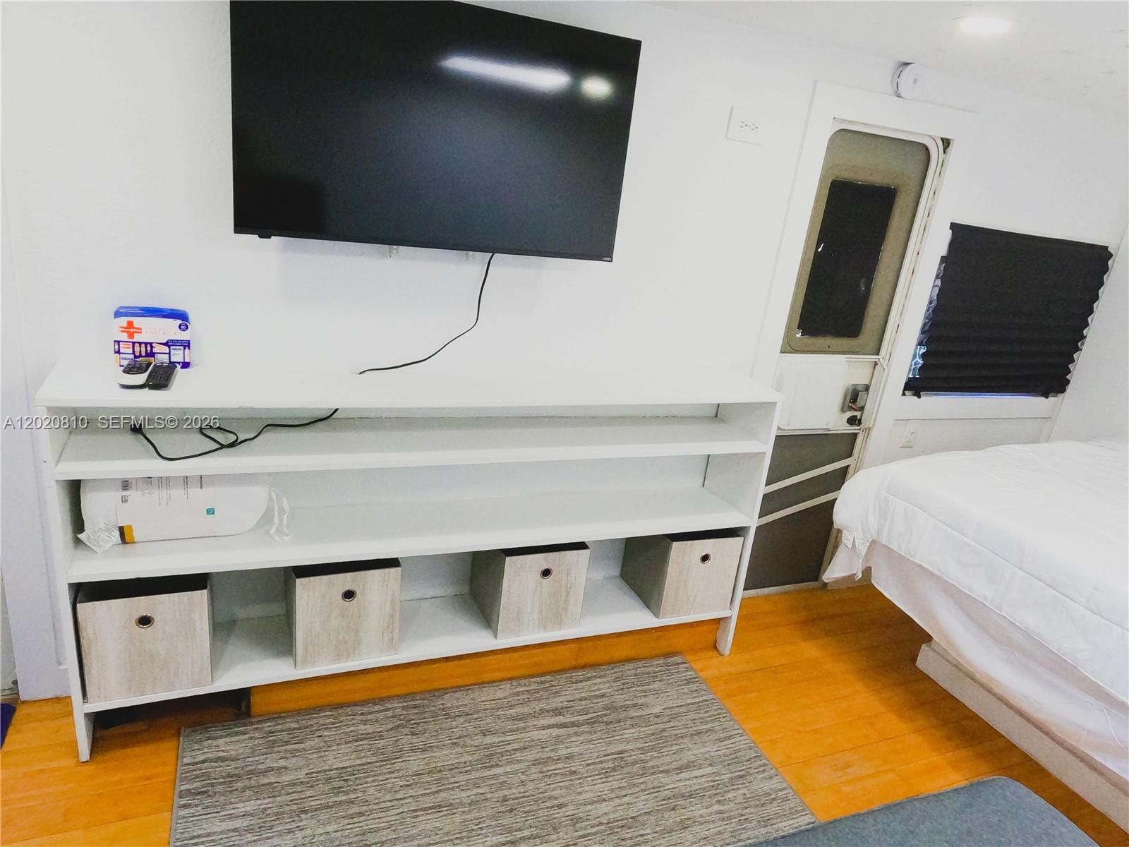 A bedroom features a wall-mounted television, a white shelving unit with storage bins, and a bed — KEY LARGO, FL