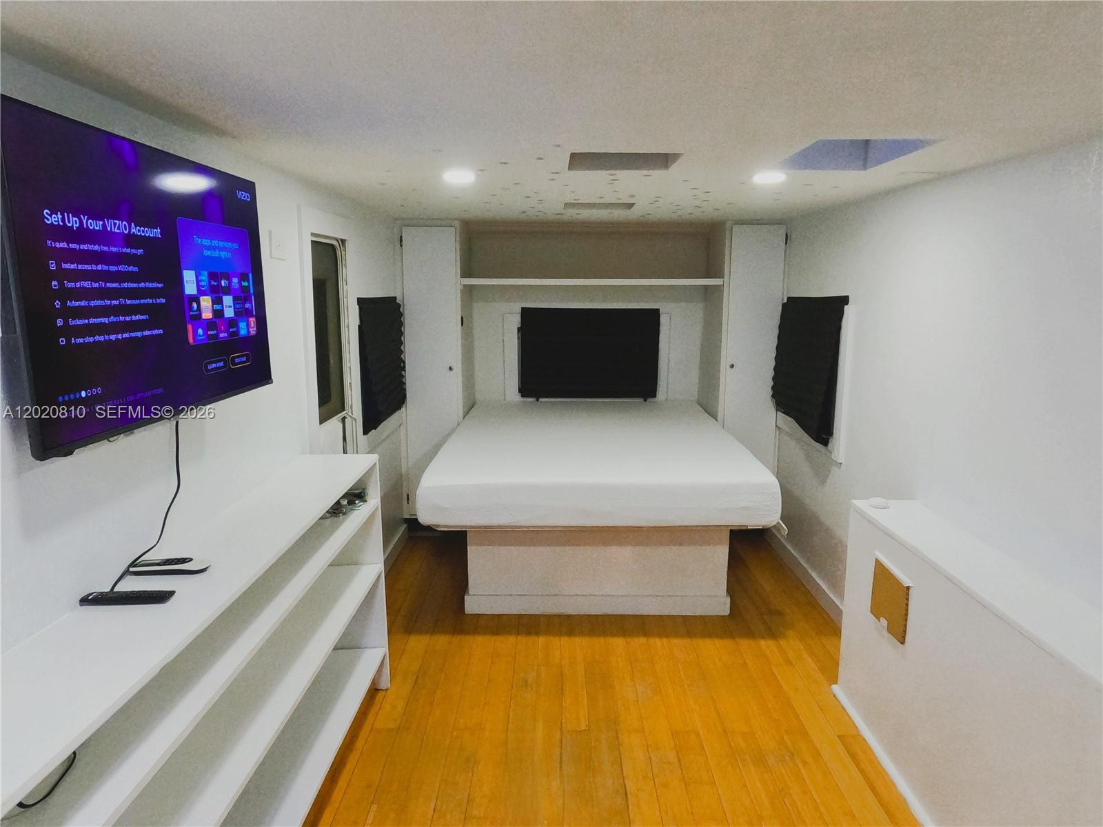 A bedroom features a bed, built-in storage, a wall-mounted television, and hardwood flooring — KEY LARGO, FL