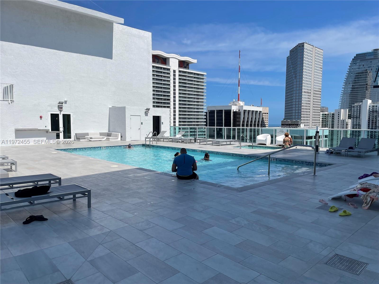 A rooftop swimming pool area features lounge chairs, light-colored tile decking, and city skyline views — 133 NE 2nd Ave # 1007, Miami FL 33132, MIAMI, FL
