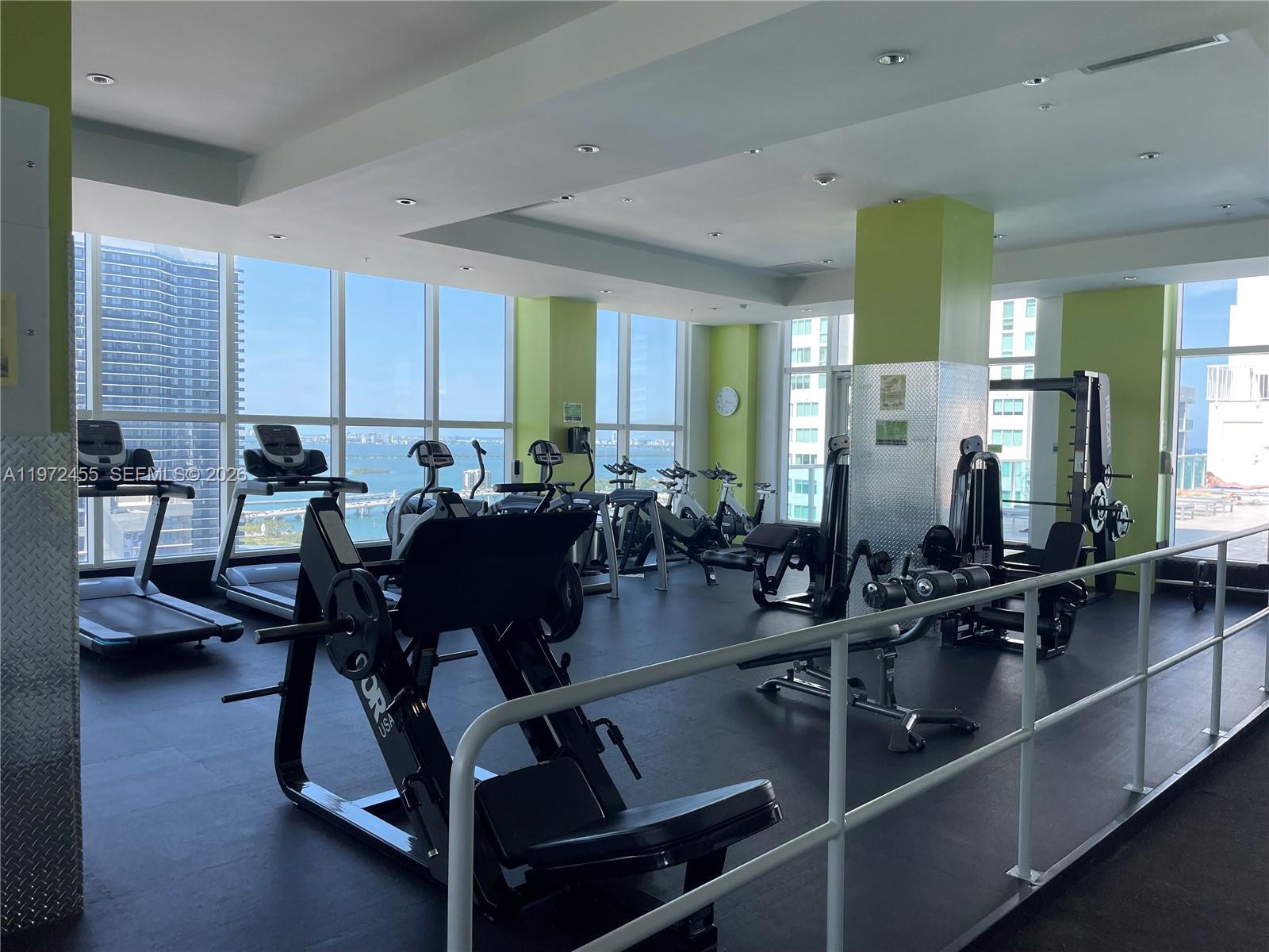 A gym features exercise equipment, floor-to-ceiling windows, and views of the ocean and city — 133 NE 2nd Ave # 1007, Miami FL 33132, MIAMI, FL