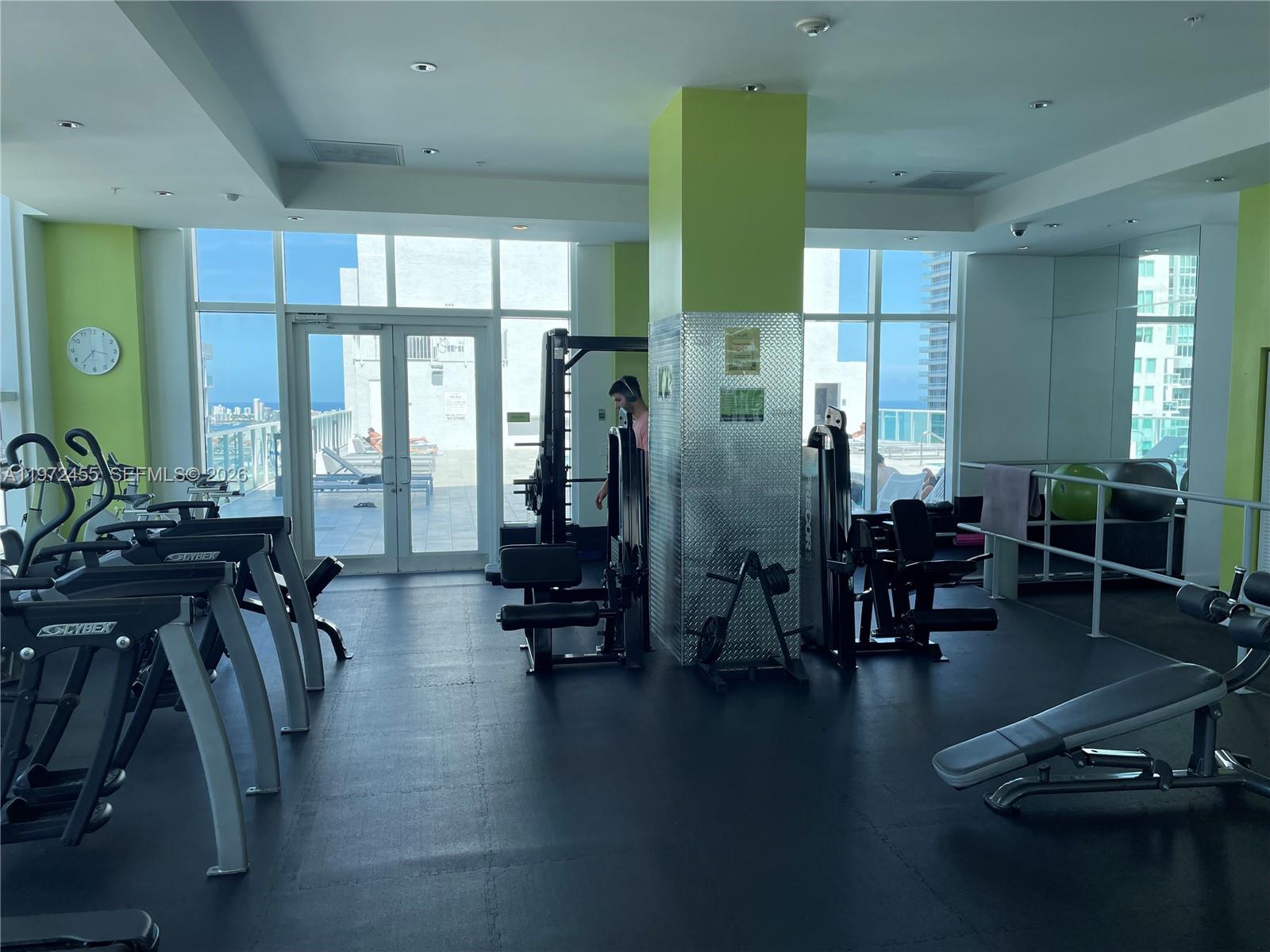 A gym features exercise equipment, a lime green pillar, and glass doors leading to a balcony — 133 NE 2nd Ave # 1007, Miami FL 33132, MIAMI, FL