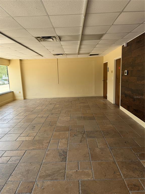 An empty commercial space features tan tile flooring, a drop ceiling, and a wood-paneled wall — 4333 SILVER STAR ROAD UNIT 155, ORLANDO, FL