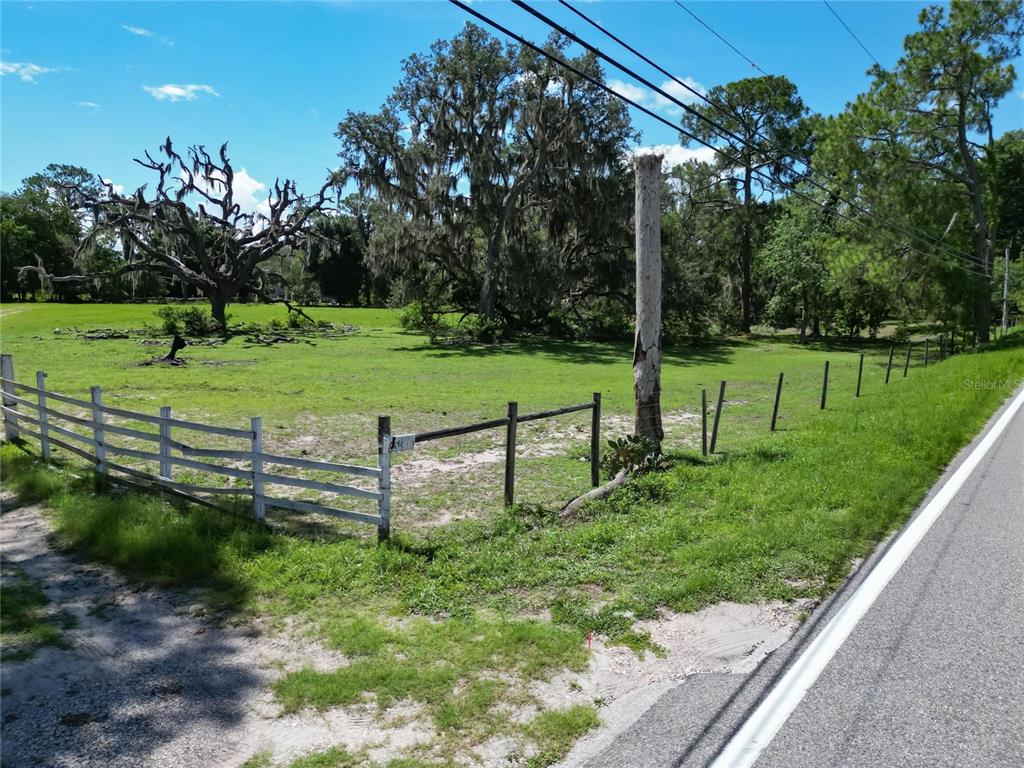 A grassy, fenced lot features large oak trees and a utility pole along a road — 8315 TOM COSTINE ROAD, LAKELAND, FL