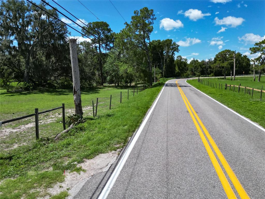 A paved road with double yellow lines runs alongside a grassy field with a fence — 8315 TOM COSTINE ROAD, LAKELAND, FL
