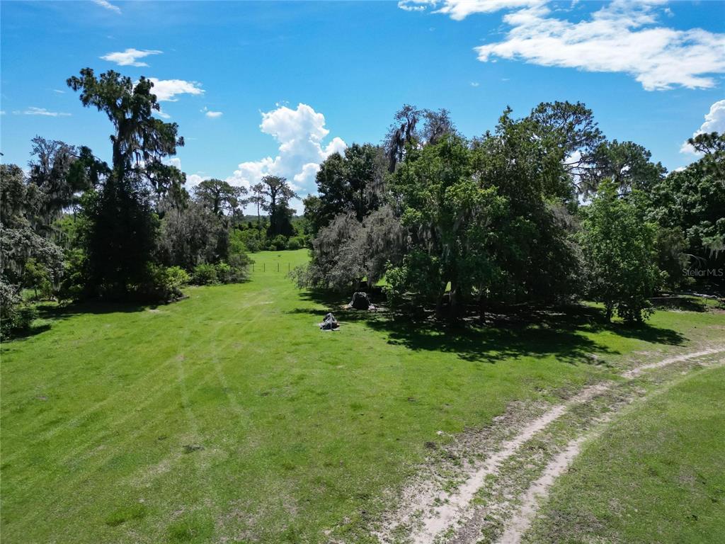 An aerial view of a grassy field surrounded by mature trees under a blue sky — 8315 TOM COSTINE ROAD, LAKELAND, FL