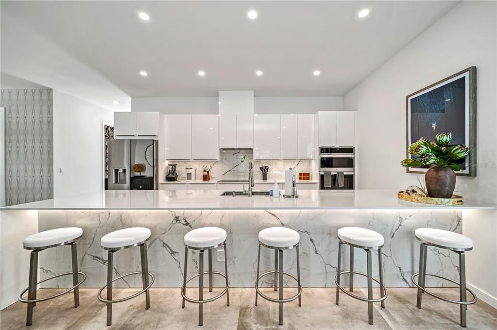 A modern kitchen features white cabinets, a marble-topped island with six stools, and recessed lighting — 2327 HILLVIEW STREET, SARASOTA, FL