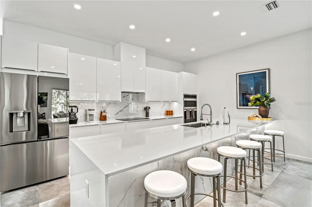 A modern kitchen features white glossy cabinets, a marble-topped island with stools, and stainless appliances — 2327 HILLVIEW STREET, SARASOTA, FL
