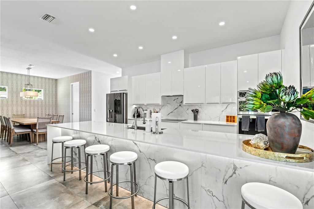 A modern kitchen features white cabinetry, marble countertops, a waterfall island, and bar stool seating — 2327 HILLVIEW STREET, SARASOTA, FL