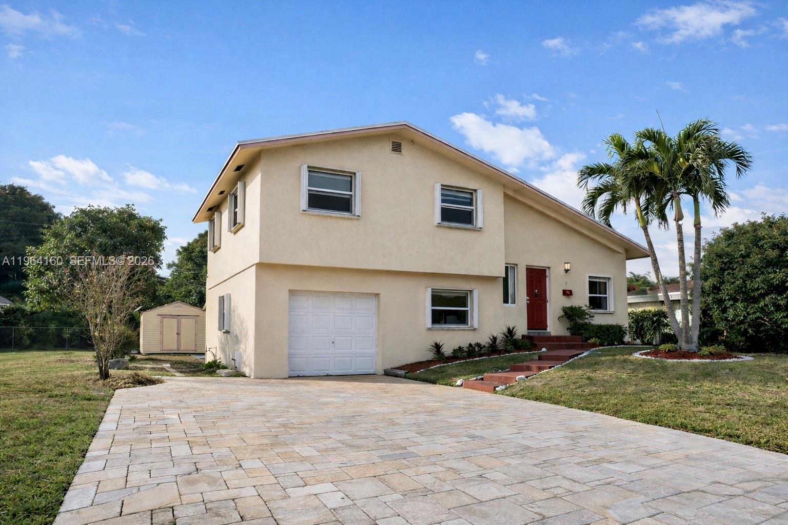 A two-story beige house with a paved driveway, a red front door, and palm trees — 640 NW 16th St, Pompano Beach FL 33060, POMPANO BEACH, FL