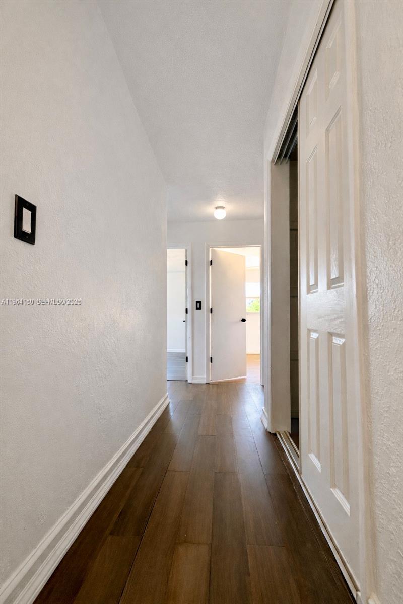 A hallway with wood-look flooring leads to two open doorways and a sliding closet door — 640 NW 16th St, Pompano Beach FL 33060, POMPANO BEACH, FL
