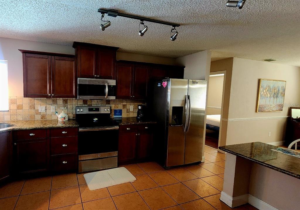 A kitchen features dark wood cabinets, stainless steel appliances, granite countertops, and tiled flooring — 10 BLACKFOOT COURT, PALM COAST, FL