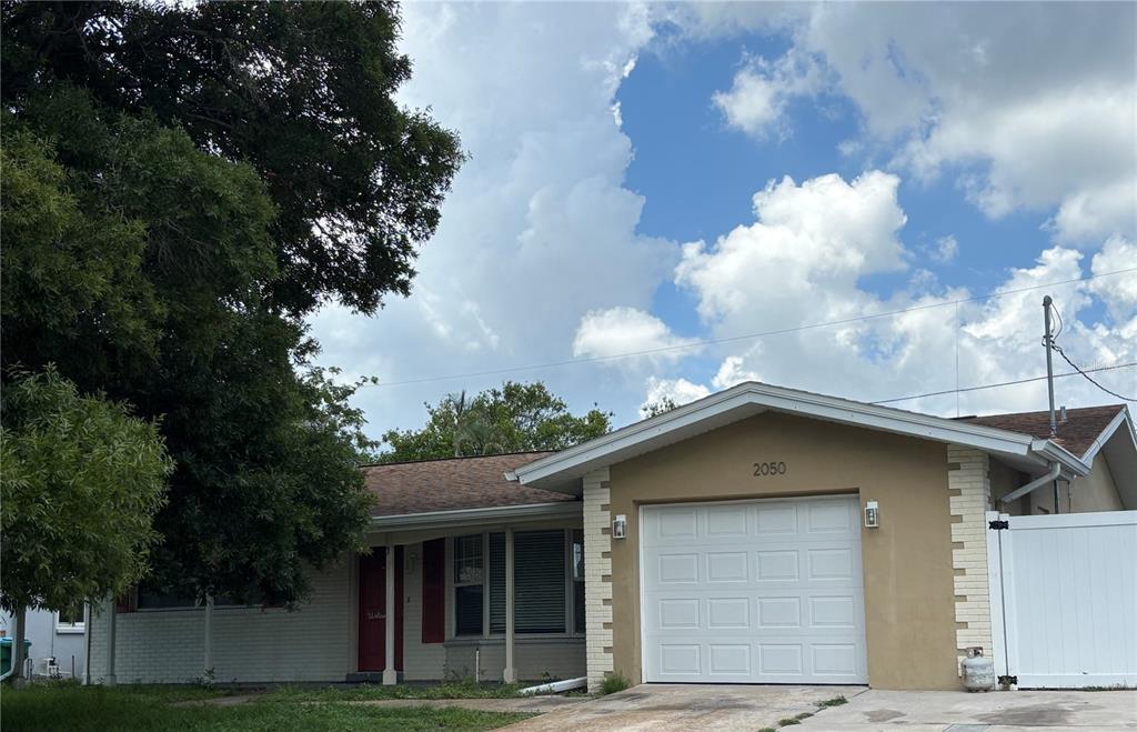 A single-story house with a white garage door, tan stucco walls, and a red front door — 2050 HIGH RIDGE DRIVE, CLEARWATER, FL