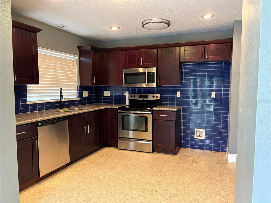 A kitchen features dark wood cabinets, stainless steel appliances, granite countertops, and blue tile backsplashes — 2050 HIGH RIDGE DRIVE, CLEARWATER, FL
