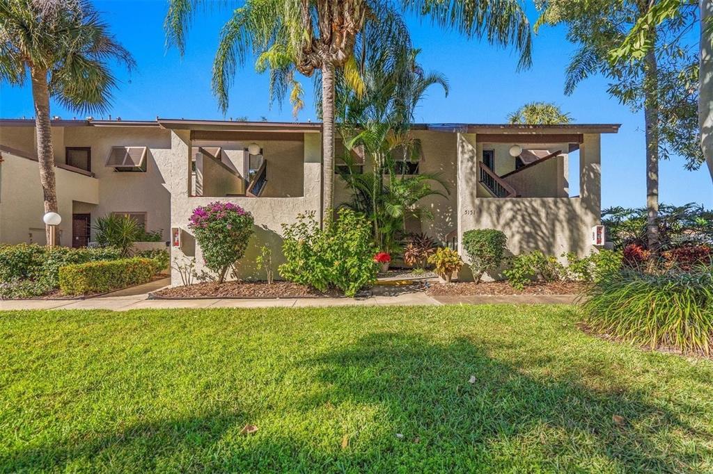 A two-story tan apartment building with a grassy lawn, palm trees, and covered entryways — 5147 WILLOW LINKS UNIT 18, SARASOTA, FL