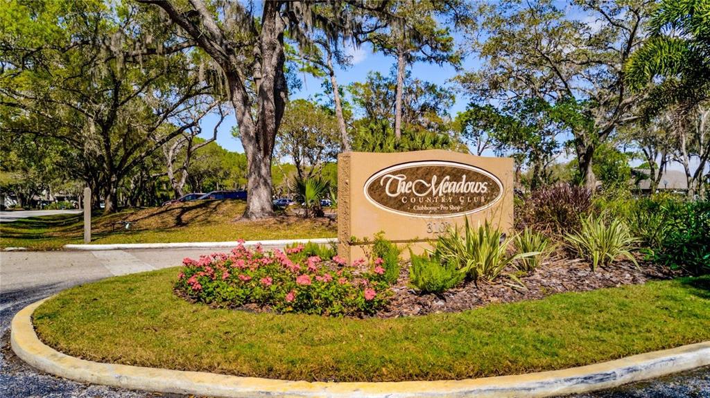 A sign for The Meadows Country Club stands in a landscaped garden with mature trees — 5147 WILLOW LINKS UNIT 18, SARASOTA, FL