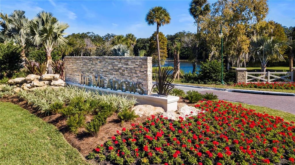A stone monument sign for The Meadows stands in a landscaped garden with red flowers — 5147 WILLOW LINKS UNIT 18, SARASOTA, FL