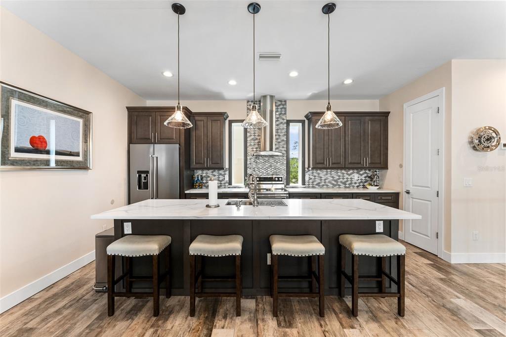 A kitchen features dark wood cabinets, a white quartz island with four stools, and pendant lighting — 4910 W MCELROY AVENUE UNIT 6, TAMPA, FL