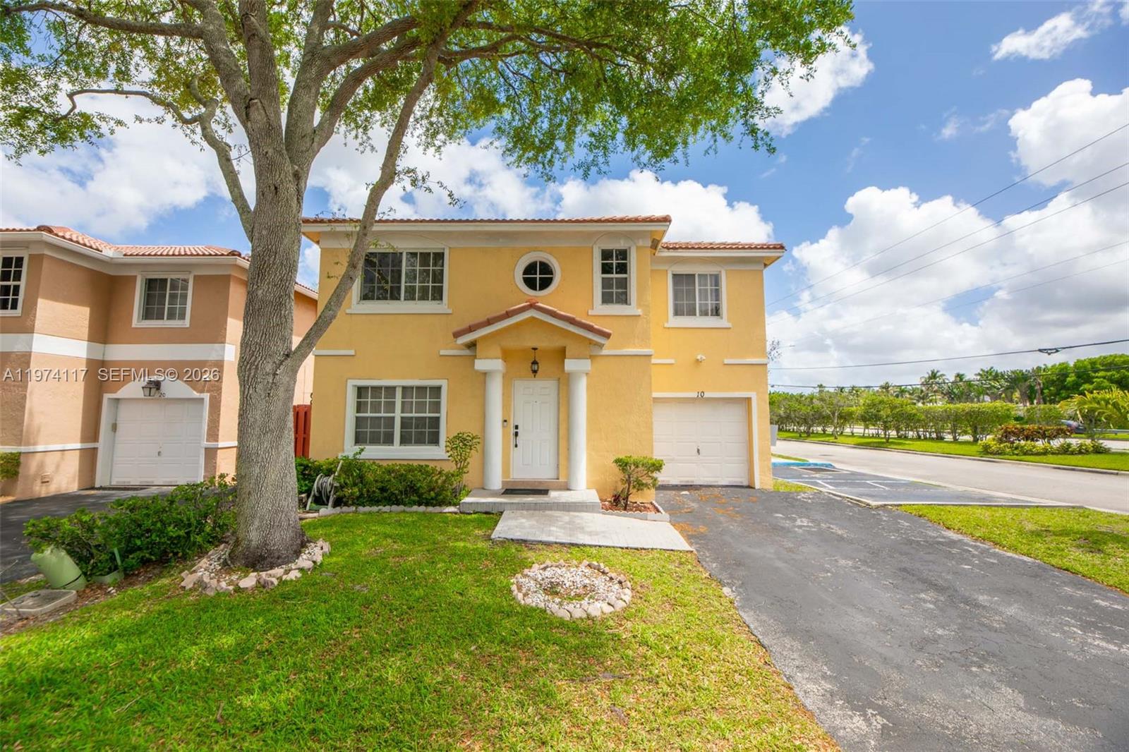 A two-story yellow stucco house features a front-facing garage, a tree, and a driveway — 10 NW 110th Ave, Plantation FL 33324, PLANTATION, FL