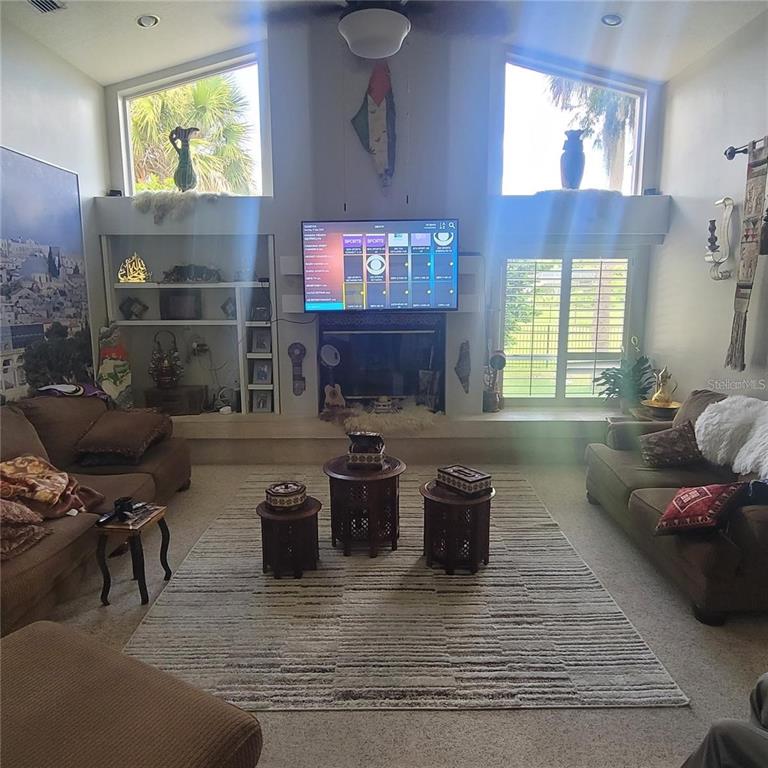 A living room features a fireplace, a wall-mounted television, built-in shelving, and large windows — 2391 WINDWARD COVE, KISSIMMEE, FL