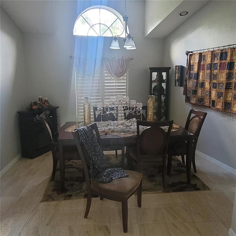 A dining room features a dark wood table, chairs, a chandelier, and a large window — 2391 WINDWARD COVE, KISSIMMEE, FL