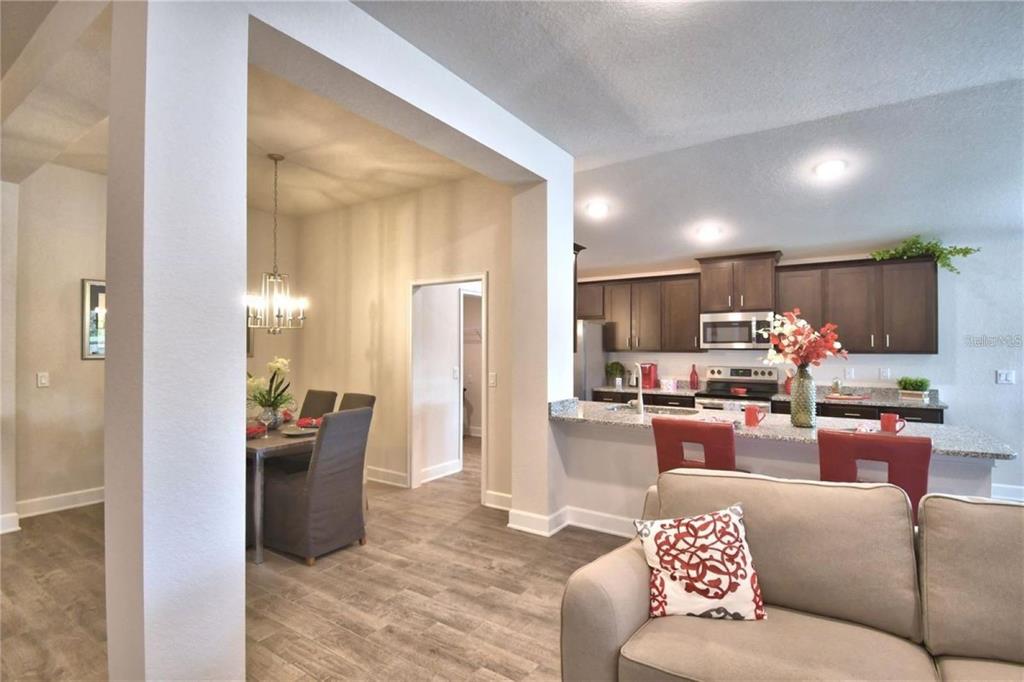 An open-concept living area features a kitchen with dark cabinets, a dining space, and wood-look flooring — 2413 NW 23RD AVENUE, OCALA, FL