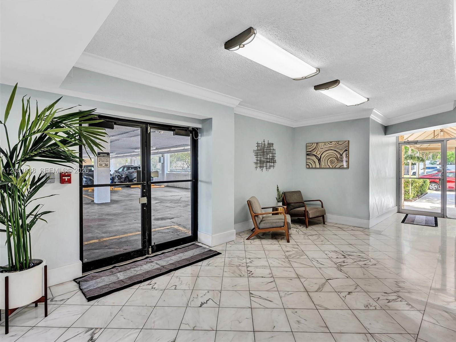 A lobby with marble-patterned tile floors, two armchairs, and glass doors leading to a parking garage — 2020 NE 135th St # 601, North Miami FL 33181, NORTH MIAMI, FL